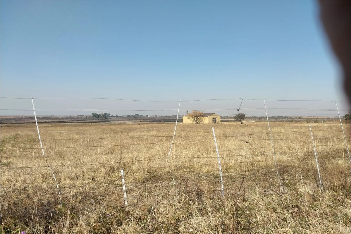 A view of the small holding property featuring open veld, wire perimeter fencing, and a distant outbuilding structure.