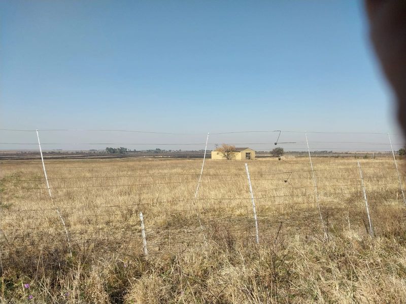 A view of the small holding property featuring open veld, wire perimeter fencing, and a distant outbuilding structure.