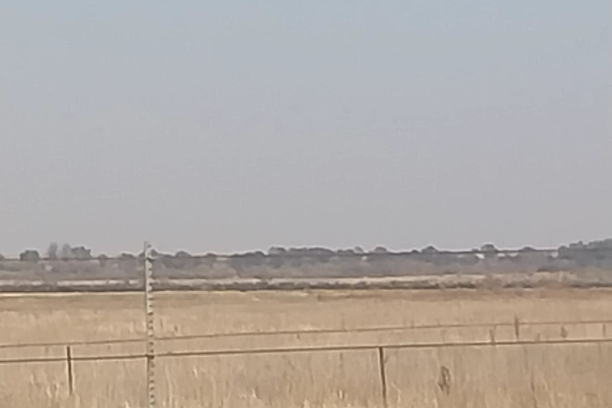 A wide-angle view of the open landscape and surrounding fields, featuring basic wire fencing along the property boundary.