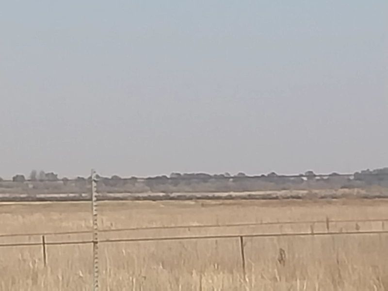 A wide-angle view of the open landscape and surrounding fields, featuring basic wire fencing along the property boundary.