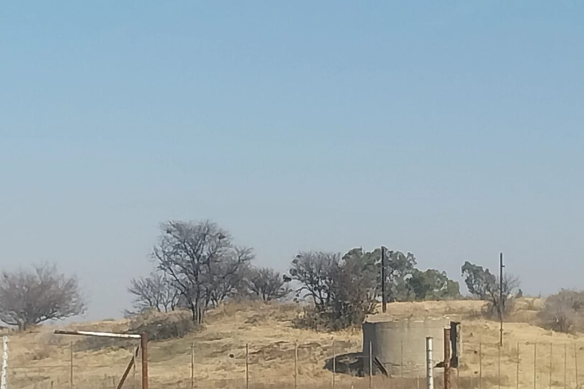 A view of the small holding landscape featuring a concrete water reservoir, wire fencing, and dry natural vegetation under a clear sky.