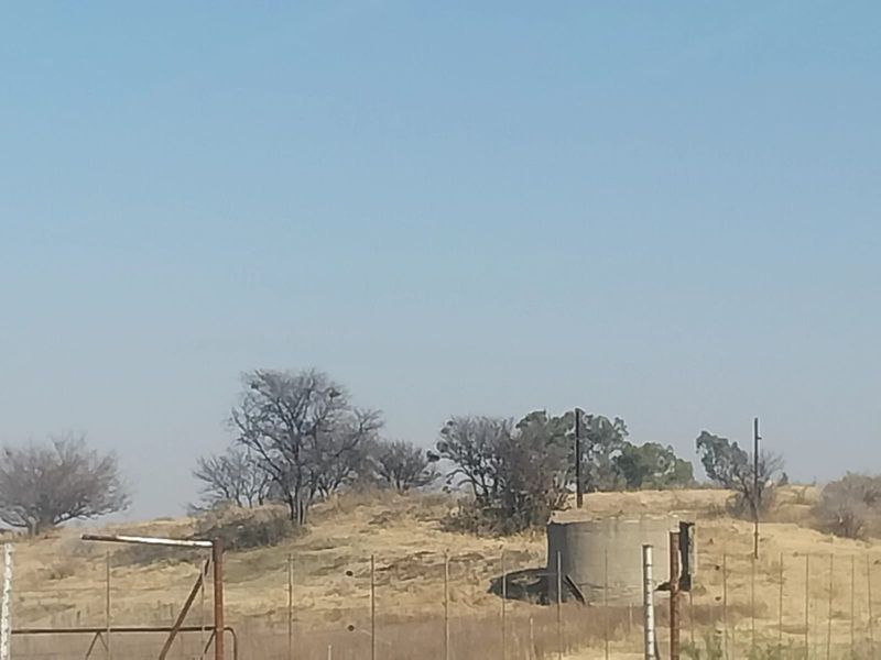 A view of the small holding landscape featuring a concrete water reservoir, wire fencing, and dry natural vegetation under a clear sky.