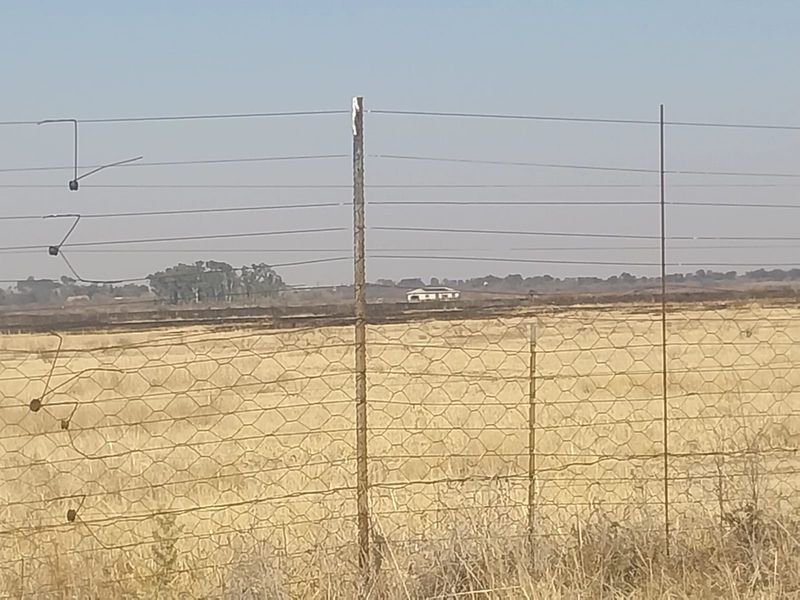 A distant view of the property landscape featuring dry veld and wire perimeter fencing.