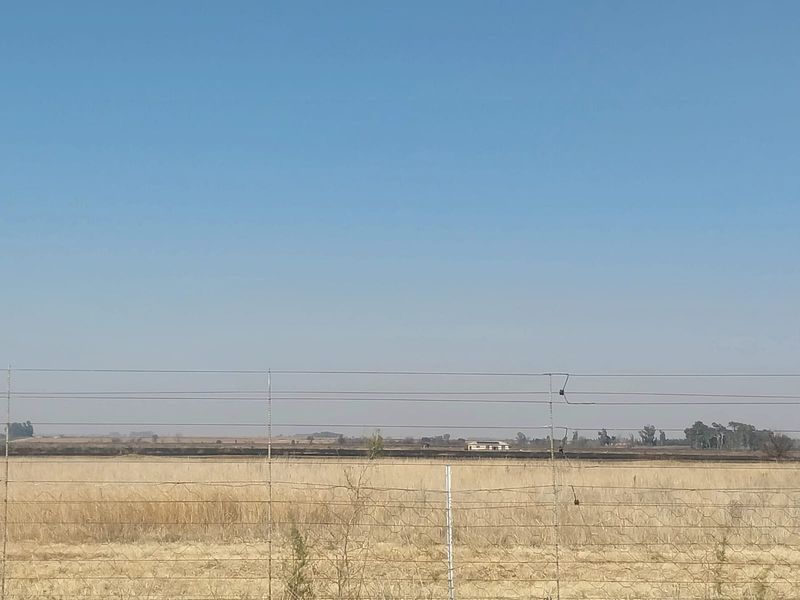 A wide-angle view of the open small holding landscape, featuring wire fencing in the foreground and distant property structures.