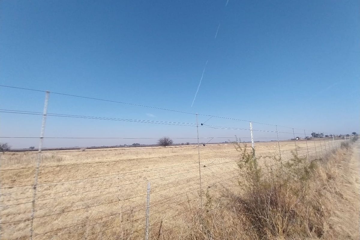 A view of the open field and surrounding land, secured by a perimeter wire and electric fence.