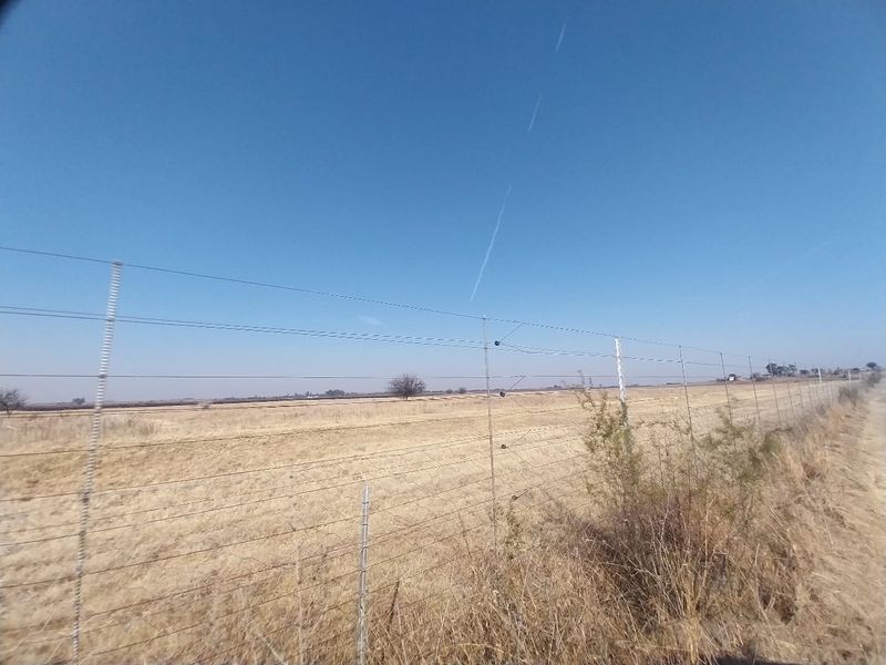 A view of the open field and surrounding land, secured by a perimeter wire and electric fence.
