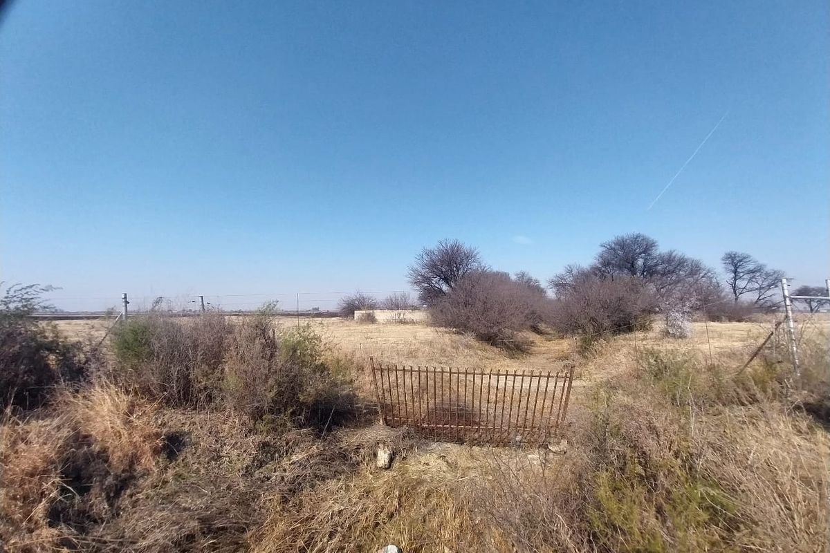 An expansive, undeveloped plot of land featuring dry vegetation, wire perimeter fencing, and a weathered metal gate entrance.