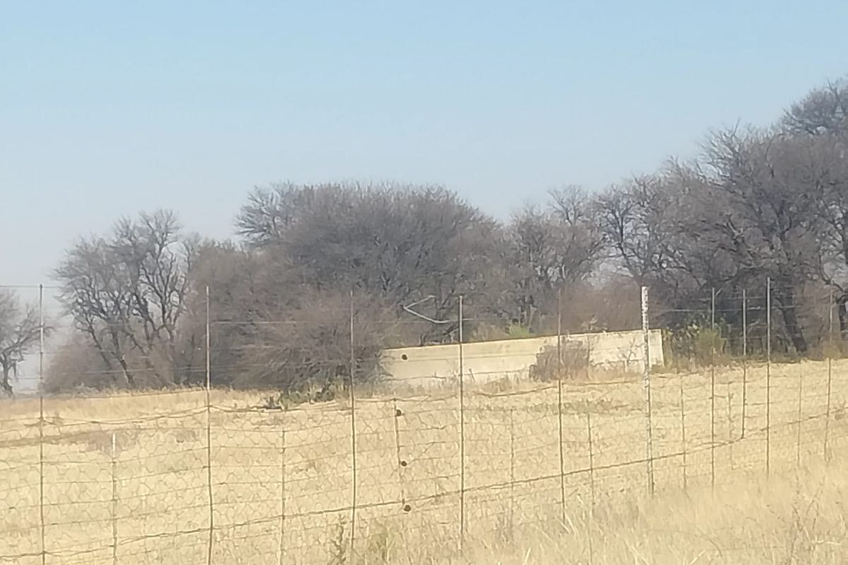 A view of the property boundary featuring wire mesh fencing and a concrete retaining wall set against a backdrop of trees.