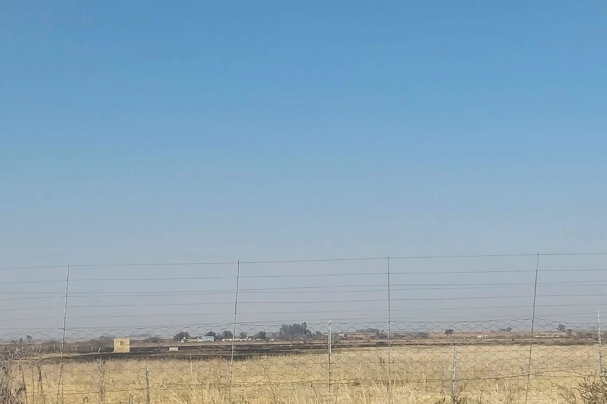 A wide-angle view of the open landscape and surrounding small holding property, featuring wire perimeter fencing and dry vegetation.