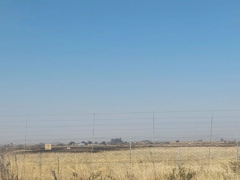 A wide-angle view of the open landscape and surrounding small holding property, featuring wire perimeter fencing and dry vegetation.