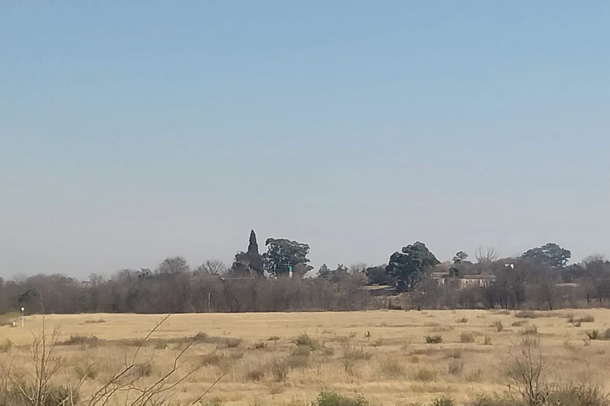 A wide landscape view of the small holding property featuring open fields and distant mature trees under a clear sky.