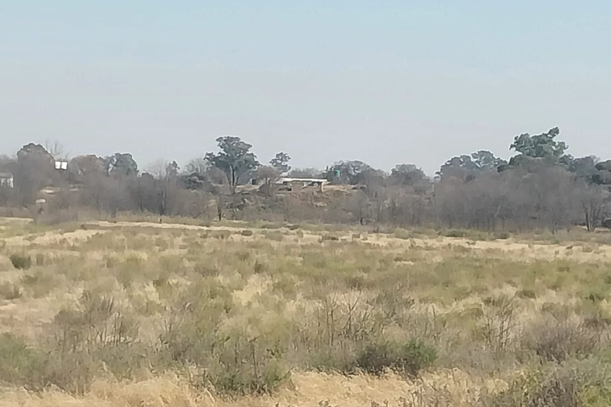 A distant view of the small holding landscape featuring open veld and natural vegetation with distant structures visible on the horizon.