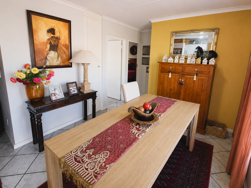 A well-maintained dining room featuring tiled flooring, coving, and a warm yellow accent wall, providing a functional space for family meals.