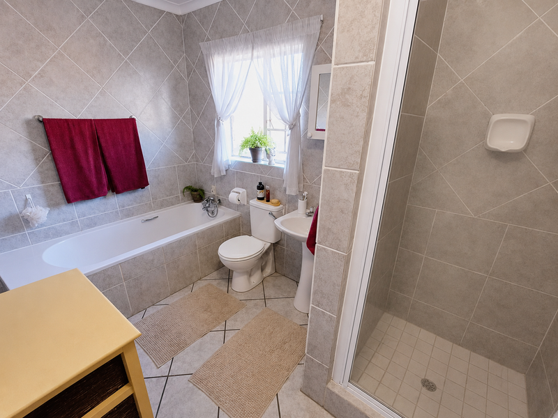 A well-maintained bathroom featuring a built-in bathtub, separate shower enclosure, pedestal sink, and neutral floor-to-ceiling wall tiling.