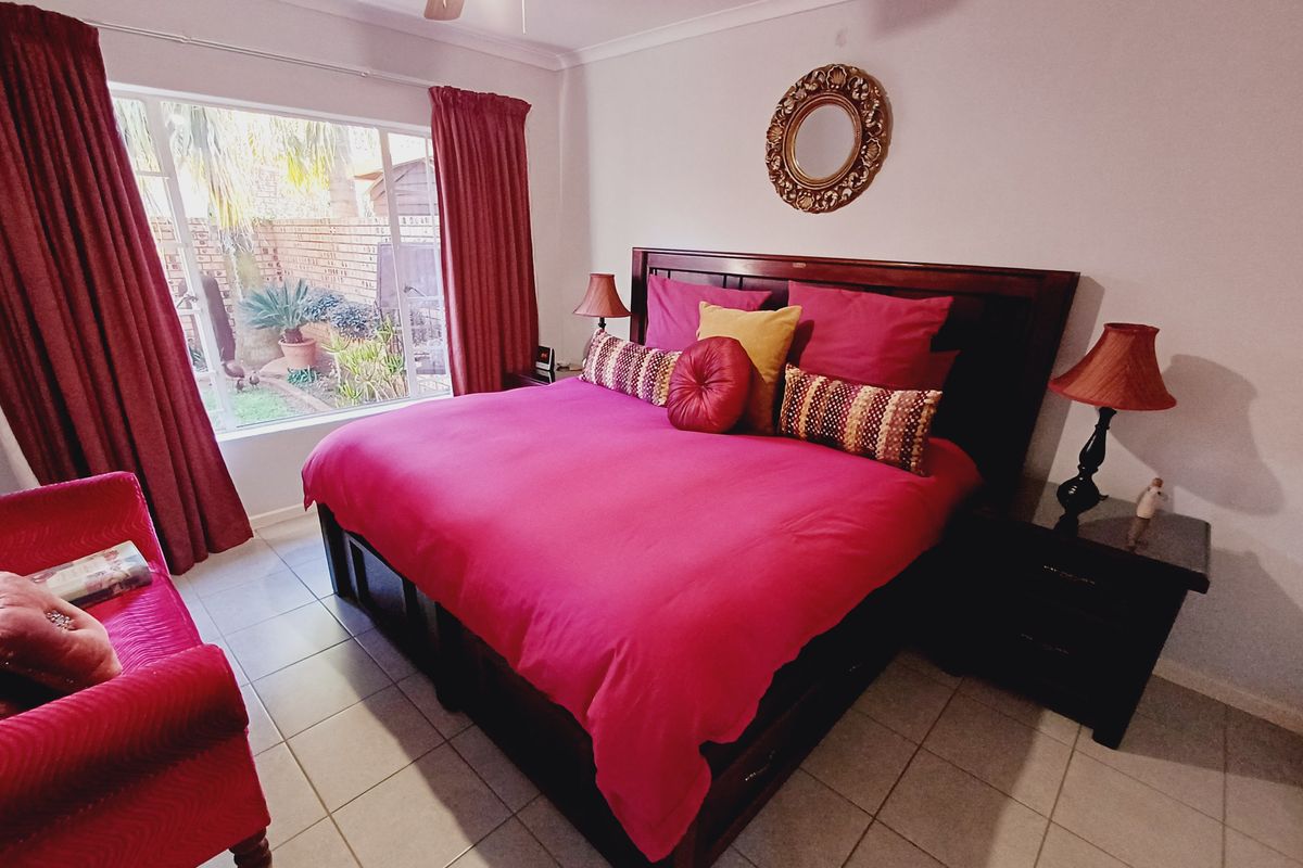 A spacious bedroom featuring tiled flooring, a ceiling fan, and a large window providing natural light and a view of the rear garden area.