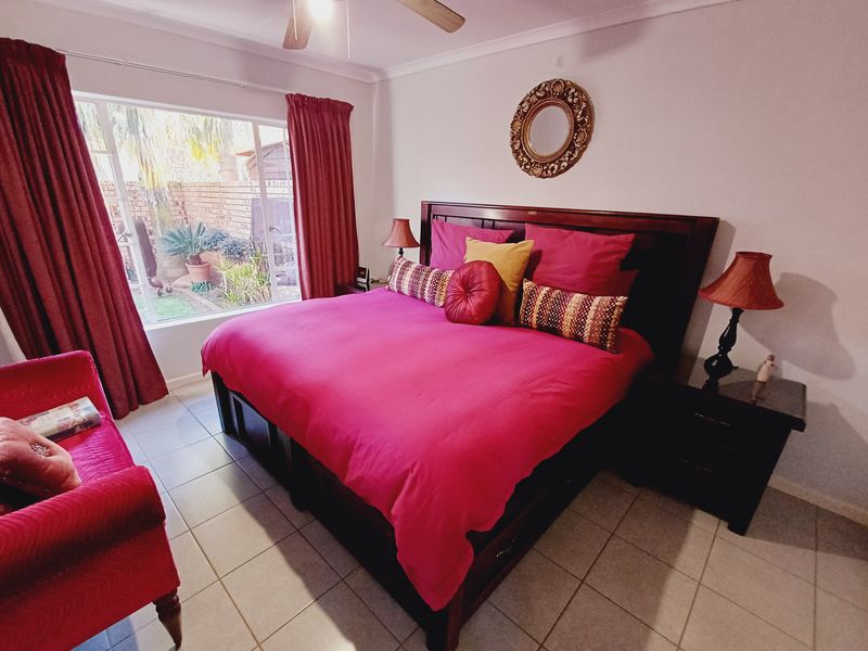 A spacious bedroom featuring tiled flooring, a ceiling fan, and a large window providing natural light and a view of the rear garden area.