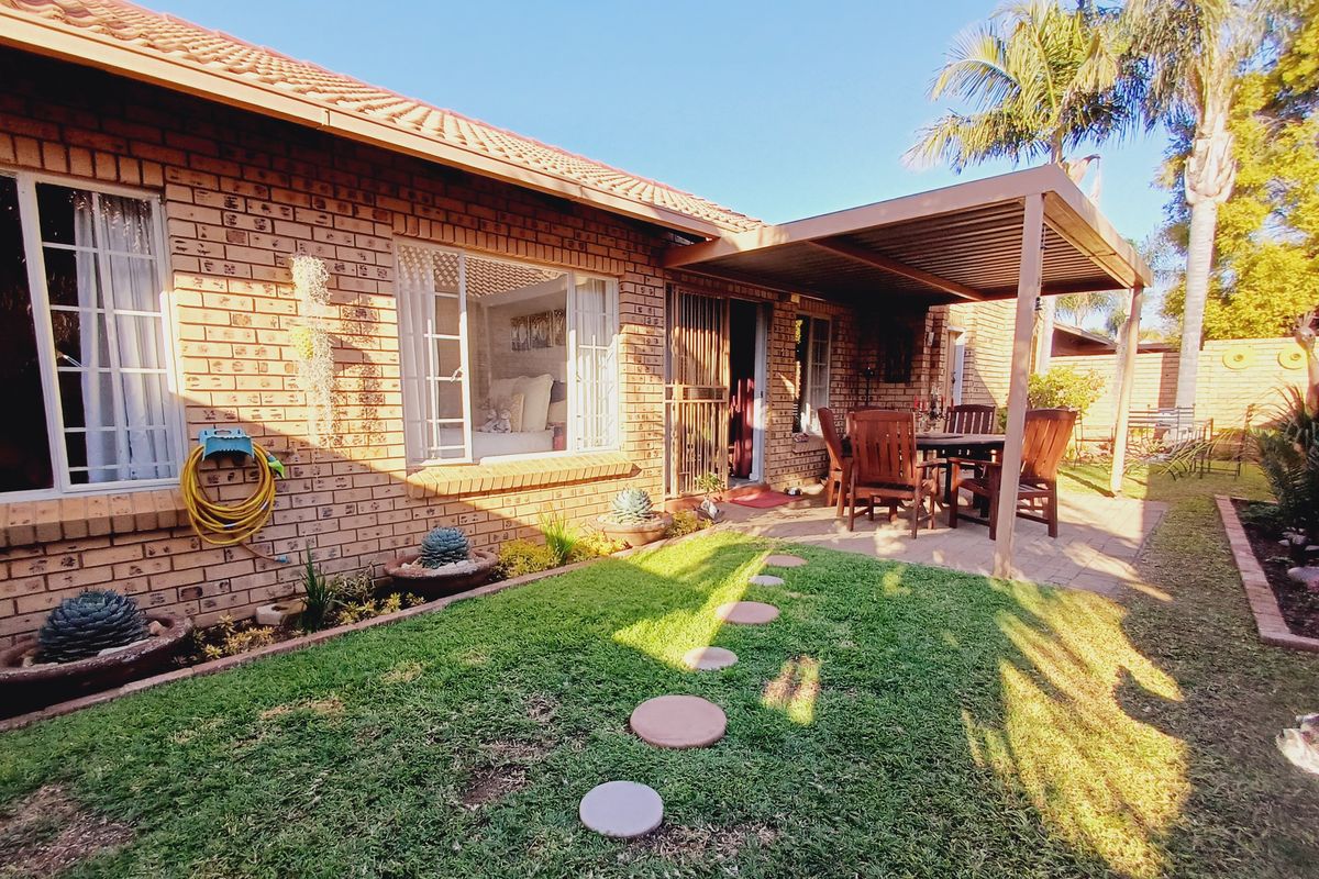 A well-maintained rear exterior featuring a brick facade, a covered patio area, and a landscaped garden with a lawn and stepping stones.