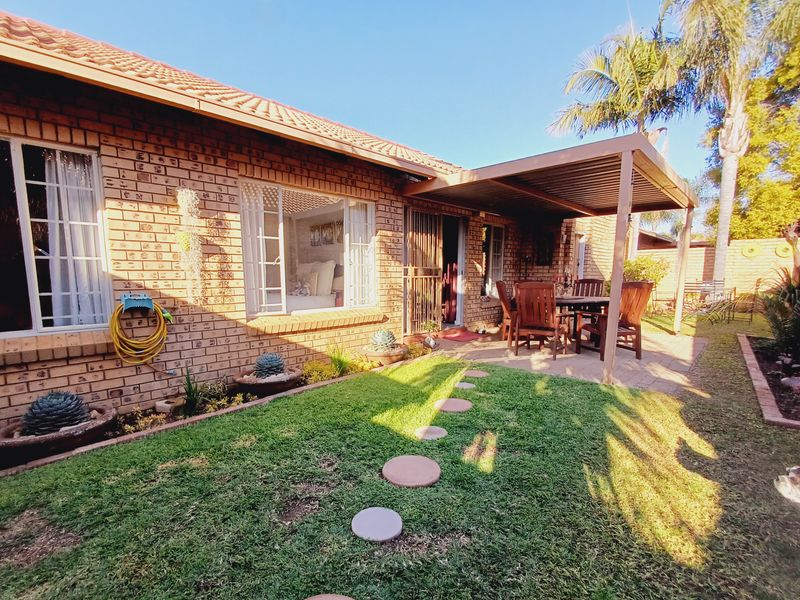 A well-maintained rear exterior featuring a brick facade, a covered patio area, and a landscaped garden with a lawn and stepping stones.