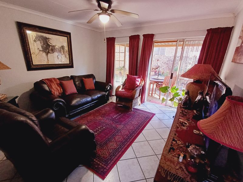 A comfortable living room featuring ceramic floor tiles, a ceiling fan, and sliding glass doors providing direct access to the outdoor patio area.