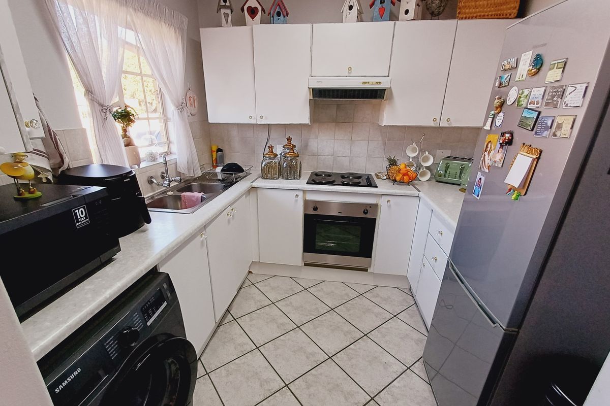 A functional U-shaped kitchen featuring white cabinetry, laminate countertops, built-in oven and hob, and tiled flooring.