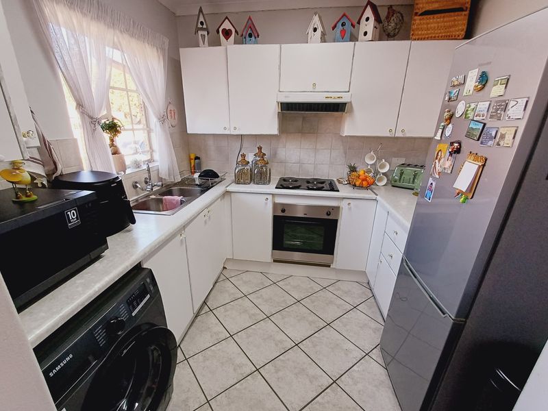 A functional U-shaped kitchen featuring white cabinetry, laminate countertops, built-in oven and hob, and tiled flooring.