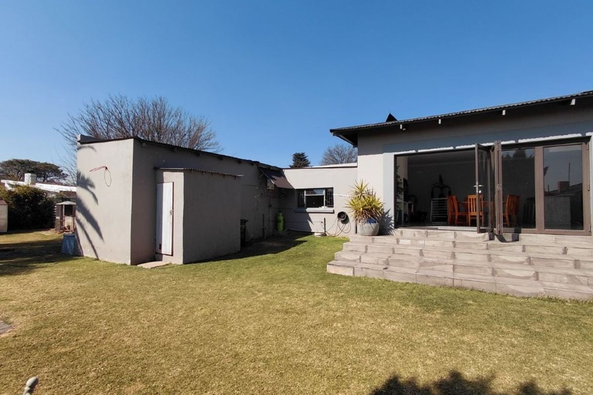 Rear view of the property featuring a lawn, tiled patio steps, and bi-fold doors leading into the living area.