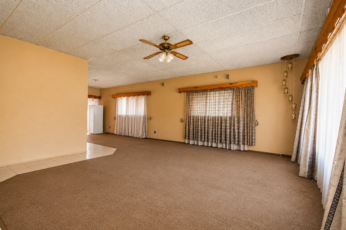 Spacious, empty living area featuring acoustic ceiling tiles, a central ceiling fan, and timber pelmets, offering a blank canvas for renovation.