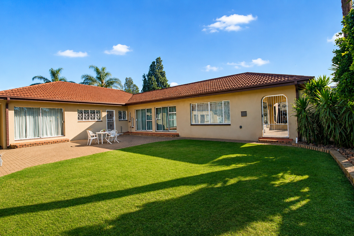 A well-maintained rear exterior view featuring a spacious lawn, paved patio area, and multiple sliding glass doors providing access to the home.