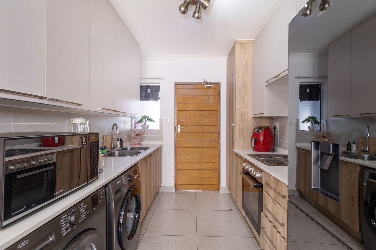 A modern, well-maintained galley kitchen featuring light-toned cabinetry, stone countertops, integrated appliances, and tiled flooring with direct access to an exterior door.