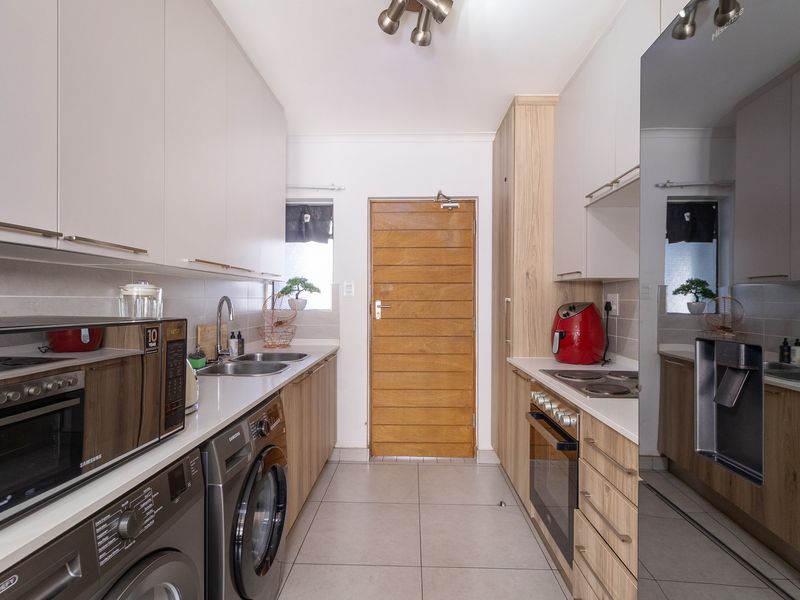 A modern, well-maintained galley kitchen featuring light-toned cabinetry, stone countertops, integrated appliances, and tiled flooring with direct access to an exterior door.