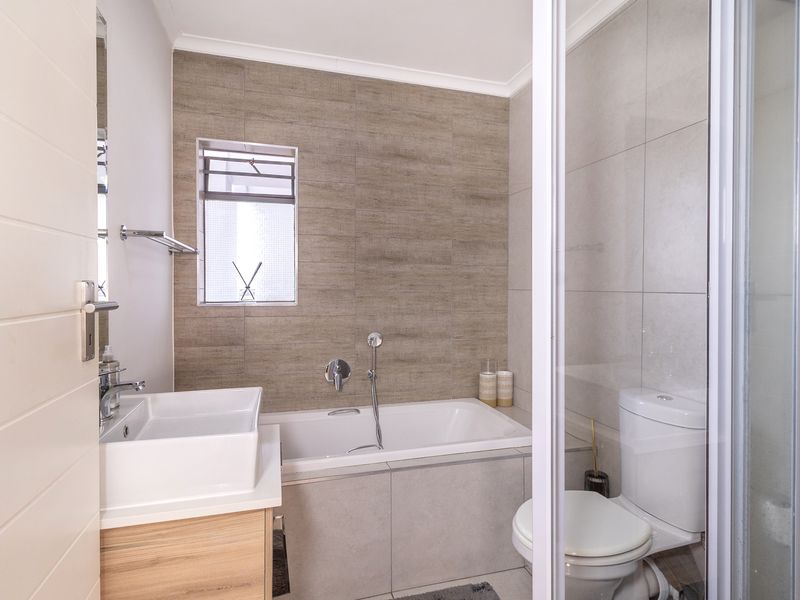 Modern bathroom featuring a built-in bathtub, separate shower enclosure, vanity basin, and neutral wall tiling.