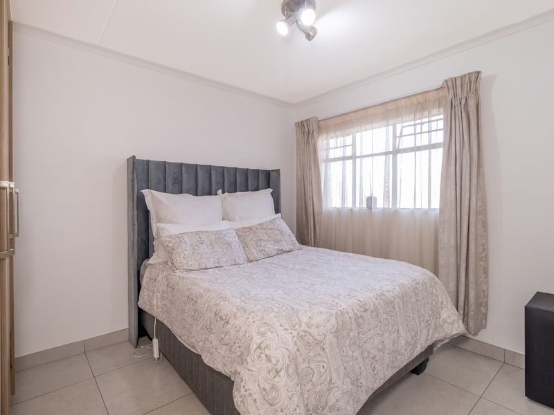 A well-maintained bedroom featuring neutral tiled flooring, a built-in wardrobe, and large windows with installed curtain tracks.