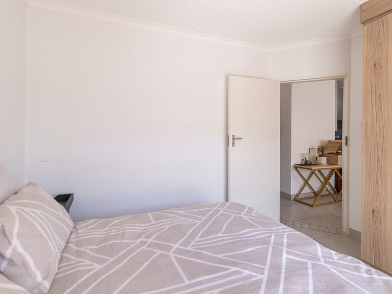 A bedroom featuring tiled flooring and a built-in wooden wardrobe, with a doorway leading to an adjacent living area.
