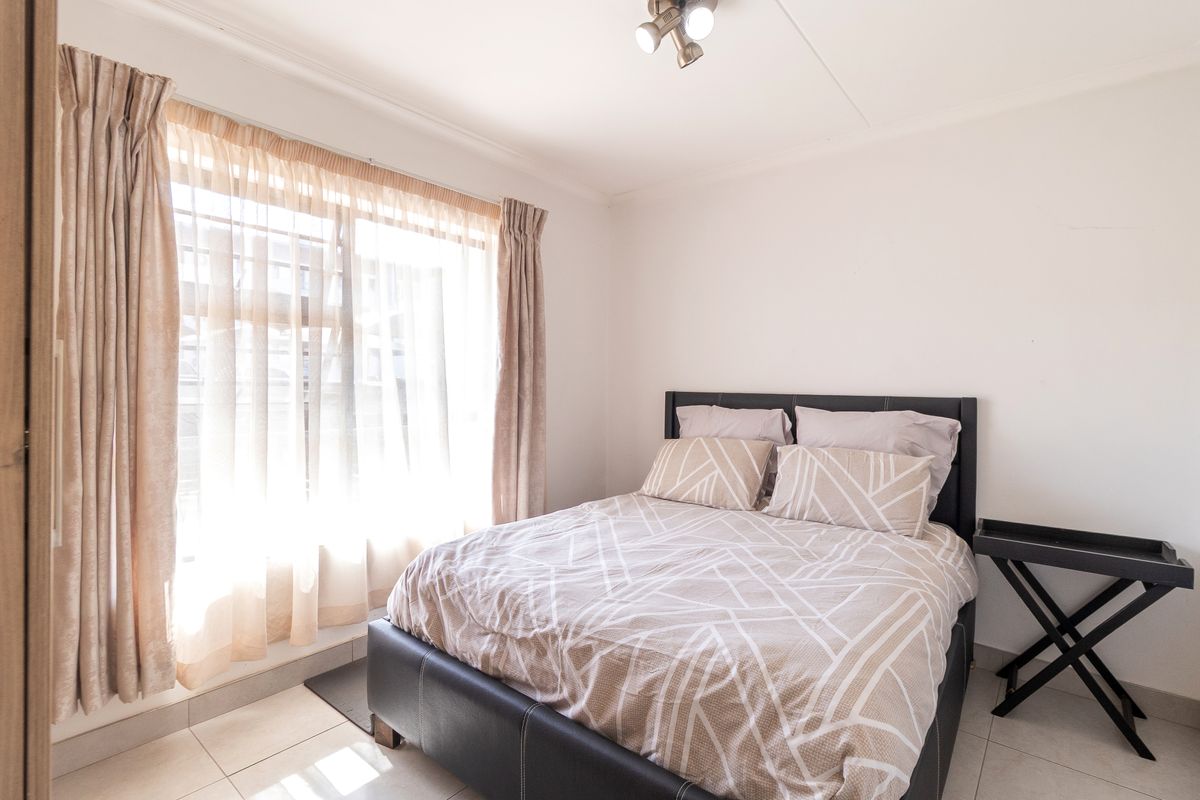 A bright bedroom featuring tiled flooring, a large window with natural light, and a ceiling-mounted spotlight fixture.