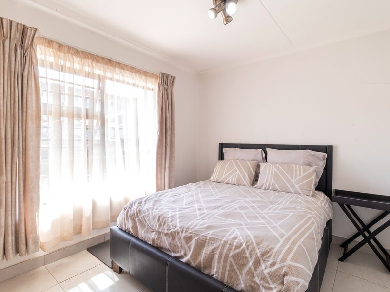 A bright bedroom featuring tiled flooring, a large window with natural light, and a ceiling-mounted spotlight fixture.