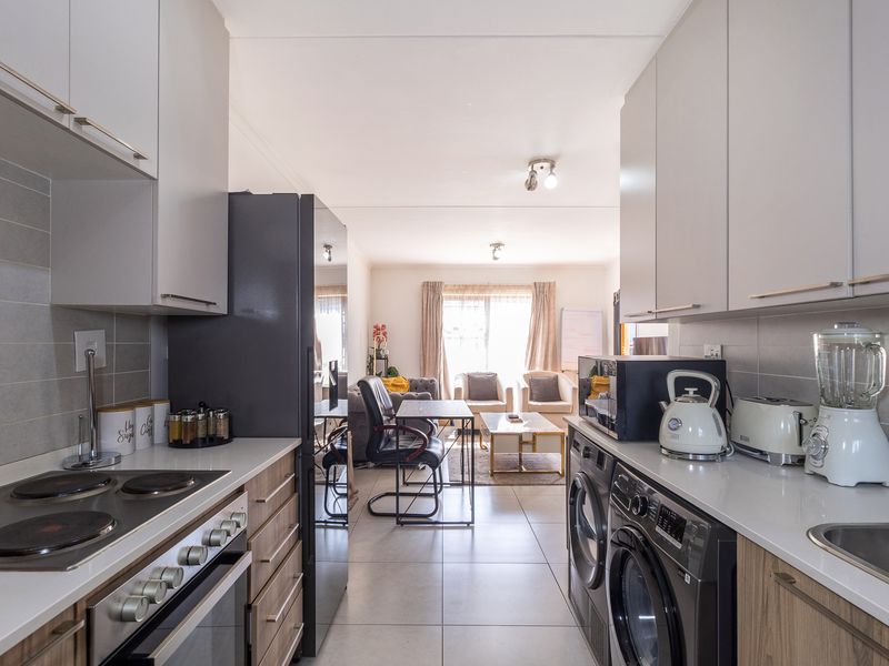 Modern open-plan kitchen and living area featuring sleek cabinetry, integrated appliances, tiled flooring, and a seamless flow to the adjacent lounge space.