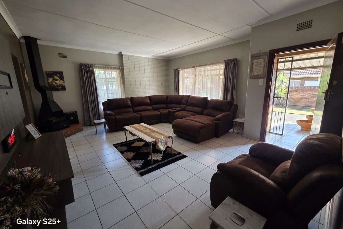 Spacious living room featuring tiled flooring, a brick feature wall, and a freestanding fireplace, with direct access to the outdoor area.