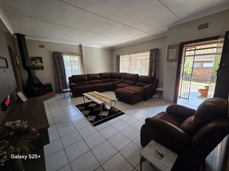 Spacious living room featuring tiled flooring, a brick feature wall, and a freestanding fireplace, with direct access to the outdoor area.