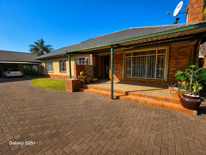 Front view of a brick house featuring a covered patio, paved driveway, and well-maintained exterior finishes.