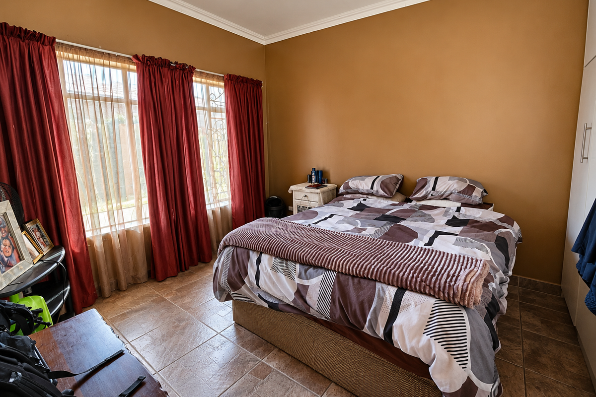 A bedroom featuring tiled flooring, built-in wardrobes, and large windows with security bars, providing a functional and well-lit living space.