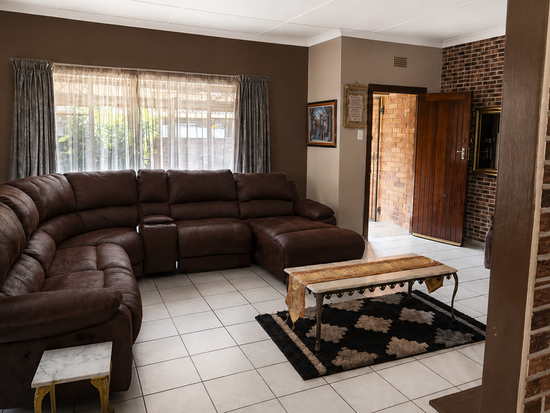 Spacious living room featuring ceramic floor tiles, an exposed brick feature wall, and direct access to an adjacent room through a wooden door.