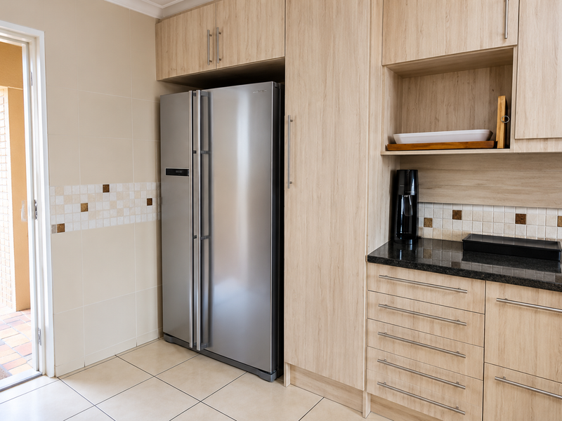 A functional scullery area featuring light wood-finish cabinetry, granite countertops, and a tiled backsplash, with direct access to an outdoor patio.