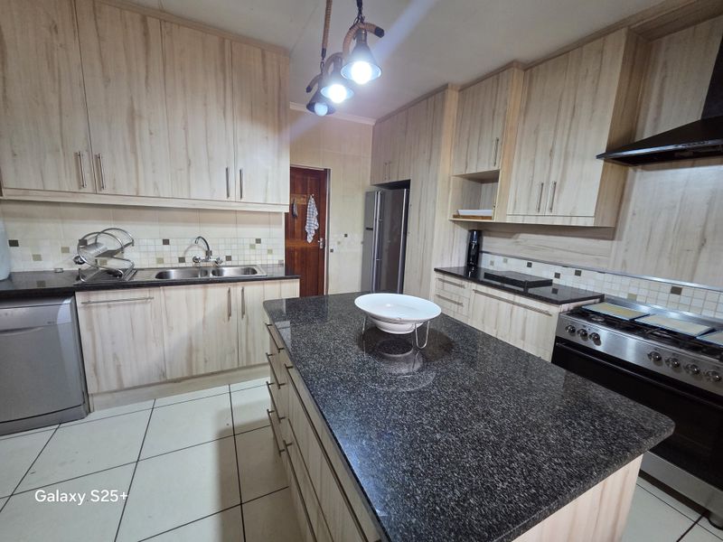 Modern kitchen featuring light wood-grain cabinetry, granite countertops, a central island, and tiled flooring with a functional layout.