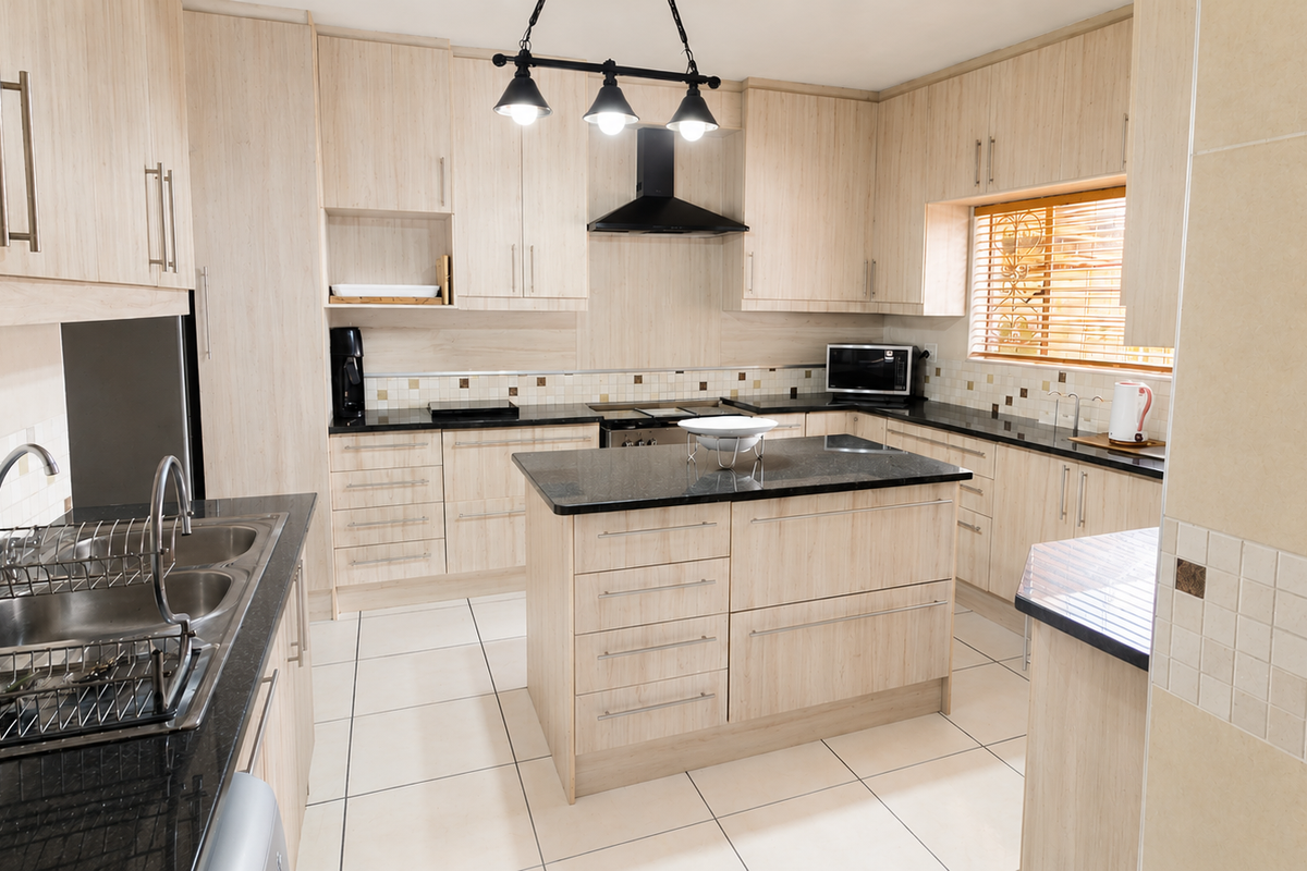 A well-maintained kitchen featuring light wood cabinetry, granite countertops, a central island, and modern tiled finishes.