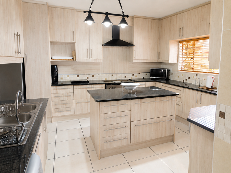 A well-maintained kitchen featuring light wood cabinetry, granite countertops, a central island, and modern tiled finishes.