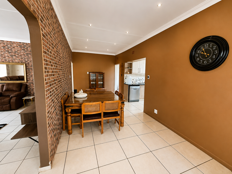 Open plan dining area featuring exposed brick feature wall, tiled flooring, and recessed lighting, with a view into the adjacent kitchen space.