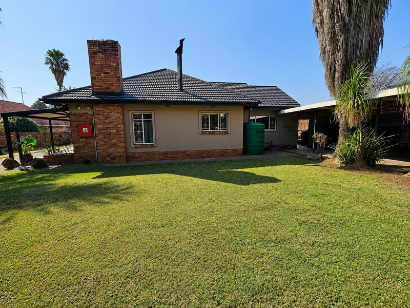 Rear view of the house featuring a brick chimney, tiled roof, water tank, and a spacious lawn area with an adjacent carport.