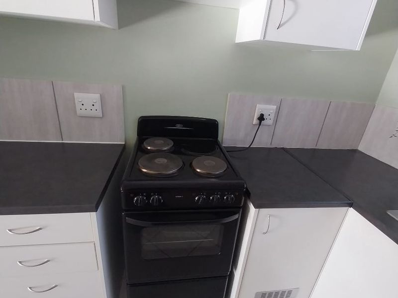 A functional kitchen area featuring white cabinetry, dark laminate countertops, a black freestanding electric stove, and neutral tiled flooring.