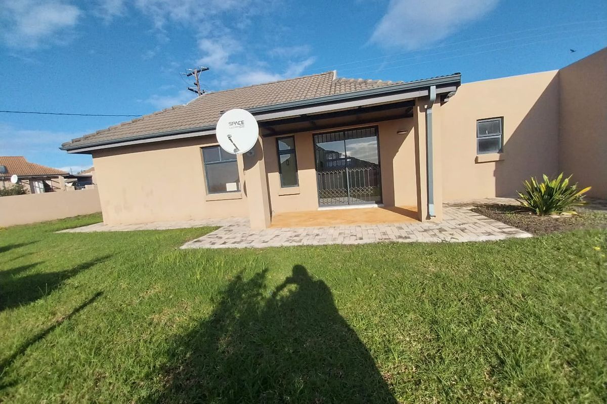 Rear view of the house featuring a paved patio area, sliding door access with security gate, and a well-maintained lawn.