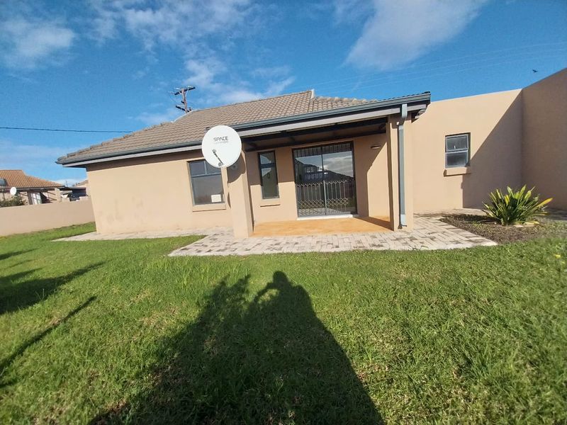 Rear view of the house featuring a paved patio area, sliding door access with security gate, and a well-maintained lawn.